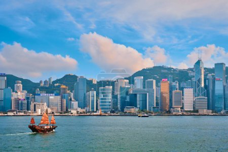 Téléchargez les photos : HONG KONG, CHINE - 1er MAI 2018 : Paysage urbain de Hong Kong gratte-ciel du centre-ville au-dessus du port de Victoria avec bateau-poubelle touristique au coucher du soleil. Hong Kong, Chine - en image libre de droit