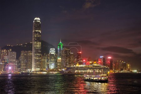 Téléchargez les photos : HONG KONG, CHINE - 1er MAI 2018 : gratte-ciel du centre-ville de Hong Kong surplombant le port de Victoria le soir illuminé par un bateau de croisière. Hong Kong, Chine - en image libre de droit