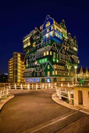 Foto de ZAANDAM, PAÍSES BAJOS - 8 DE MAYO DE 2017: Hotel Inntel en Zaandam iluminado por la noche. El diseño de un edificio de 12 plantas de altura inaugurado en 2009 es el resultado de apilar una serie de casas holandesas tradicionales. - Imagen libre de derechos
