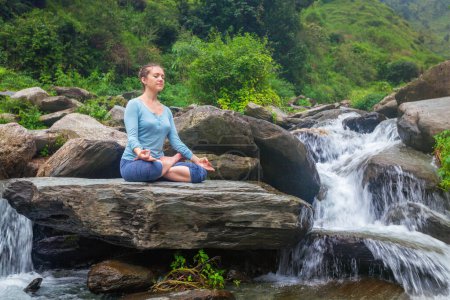 Photo for Woman doing yoga meditation asana Padmasana lotus pose outdoors at tropical waterfall - Royalty Free Image