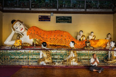 Téléchargez les photos : YANGON, MYANMAR - 3 JANVIER 2014 : Homme méditant près de la statue de Bouddha couché dans la pagode Shwedagon Paya - en image libre de droit