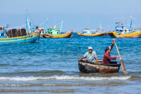 Téléchargez les photos : PHAN THIET, VIETNAM - 5 JUIN 2011 : Deux pêcheurs dans un bateau coracle revenant de la pêche. Phan Thiet est une ville côtière célèbre pour son quartier touristique Mui Ne et fruits de mer ainsi que des produits de la mer. - en image libre de droit