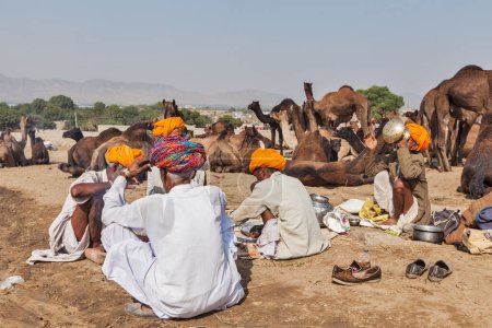 Foto de PUSHKAR, INDIA - 21 DE NOVIEMBRE DE 2012: Hombres y camellos indios en la feria de camellos de Pushkar (Pushkar Mela) - feria anual de camellos y ganado de cinco días, una de las ferias de camellos más grandes del mundo y atracción turística - Imagen libre de derechos