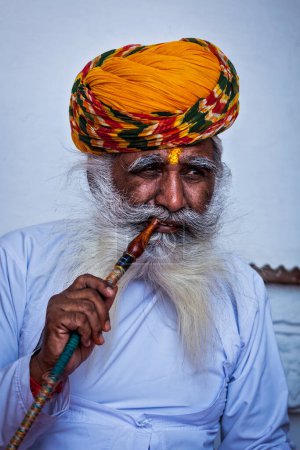 Foto de JODHPUR, INDIA - 26 de noviembre de 2012: El anciano indio fuma narguile (pipa de agua) en el fuerte de Mehrangarh. Se cree que el concepto de narguile se originó en la India. - Imagen libre de derechos