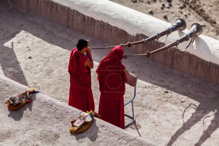 Téléchargez les photos : THIKSEY, INDE - 4 SEPTEMBRE 2011 : Deux moines bouddhistes tibétains soufflent de la corne tibétaine (dungche) pendant la matinée poja, Thiksey gompa, Ladakh, Inde - en image libre de droit