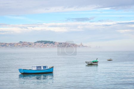 Foto de Barcos de pesca en el río Tajo en la mañana brumosa con Lisboa en el fondo con niebla. Lisboa, Portugal - Imagen libre de derechos
