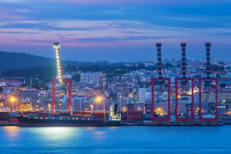 Photo for View of Lisbon port with moored sea container ship with port cranes in the evening twilight over Tagus river. Lisbon, Portugal - Royalty Free Image