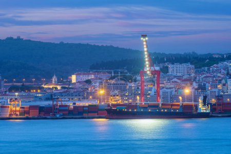 Téléchargez les photos : Vue du port de Lisbonne avec un porte-conteneurs maritime amarré avec des grues portuaires au crépuscule du soir sur le Tage. Lisbonne, Portugal - en image libre de droit