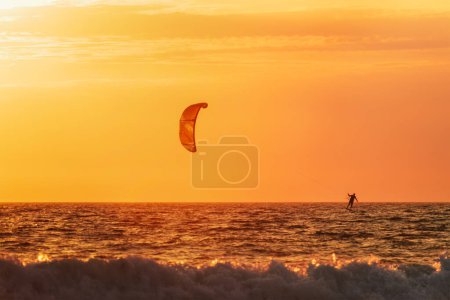 Téléchargez les photos : Foiling Kiteboard Kitesurf Kiteboarder (kitesurfer) silhouette dans l'océan Atlantique au coucher du soleil. Plage de Fonte da Telha, Costa da Caparica, Portugal - en image libre de droit