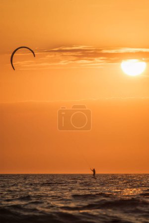 Téléchargez les photos : Foiling Kiteboard Kitesurf Kiteboarder (kitesurfer) silhouette dans l'océan Atlantique au coucher du soleil. Plage de Fonte da Telha, Costa da Caparica, Portugal - en image libre de droit