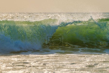 Foto de Rompiendo la ola oceánica al atardecer retroiluminado con sol. Fonte da Telha, Costa da Caparica, Portugal - Imagen libre de derechos