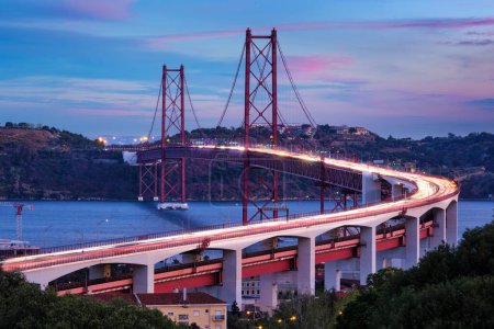 Photo for View of Lisbon view from Miradouro do Bairro do Alvito viewpoint of Tagus river, traffic with light trails on 25th of April Bridge, and Christ the King statue in the evening twilight. Lisbon, Portugal - Royalty Free Image