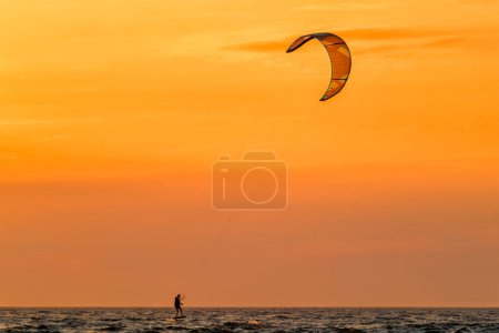 Foto de Foiling kiteboarding kitesurfing kiteboarder kitesurfer silueta en el océano Atlántico al atardecer. Fonte da Telha beach, Costa da Caparica, Portugal - Imagen libre de derechos
