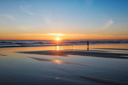Téléchargez les photos : Coucher de soleil sur l'océan Atlantique avec silhouette de photographe prenant des images des vagues sur la plage de Fonte da Telha, Costa da Caparica, Portugal - en image libre de droit