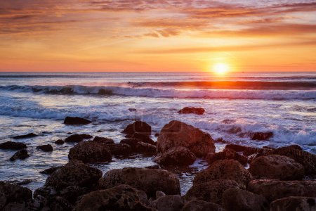 Téléchargez les photos : Coucher de soleil sur l'océan Atlantique avec vagues et rochers à Costa da Caparica, Portugal - en image libre de droit