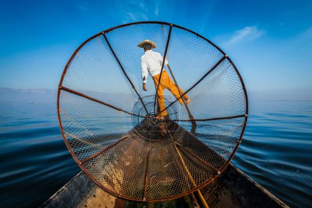 Foto de Atracción turística de Myanmar - Pescador tradicional birmano con red de pesca en el lago Inle en Myanmar famoso por su distintivo estilo de remo de una pierna, vista desde el barco - Imagen libre de derechos