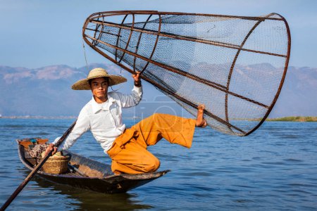 Foto de Atracción turística de Myanmar - Pescador tradicional birmano con red de pesca en el lago Inle en Myanmar famoso por su distintivo estilo de remo de una pierna - Imagen libre de derechos