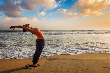 Mujer joven haciendo yoga Saludo al sol Surya Namaskar pose Hasta Uttanasana en la playa tropical al atardecer