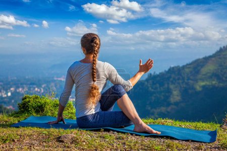 Téléchargez les photos : Hatha yoga en plein air - femme faisant du yoga asana Parivrtta Marichyasana ou ardha matsyendrasana - assis spinal torsion en plein air dans les montagnes le matin - en image libre de droit