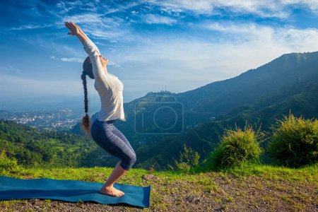 Photo for Young woman doing yoga asana Utkatasana chair pose outdoors in mountains Himalayas in the morning. Himachal Pradesh, India - Royalty Free Image