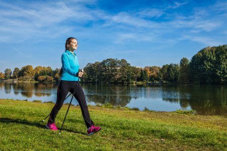 Photo for Nordic walking adventure and exercising concept - woman hiking with nordic walking poles in park - Royalty Free Image