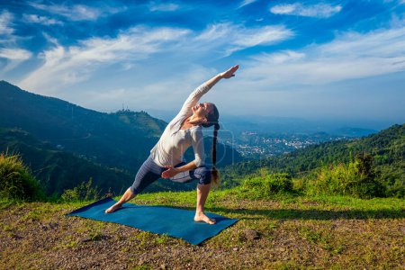 Photo for Woman practices yoga asana Utthita Parsvakonasana - extended side angle pose outdoors in mountains in the morning - Royalty Free Image