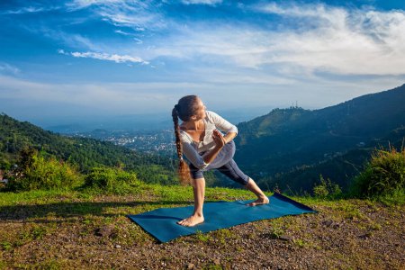 Téléchargez les photos : Femme pratique Ashtanga Vinyasa yoga asana Utthita Parsvakonasana varitation - pose d'angle latéral étendu à l'extérieur dans les montagnes le matin - en image libre de droit