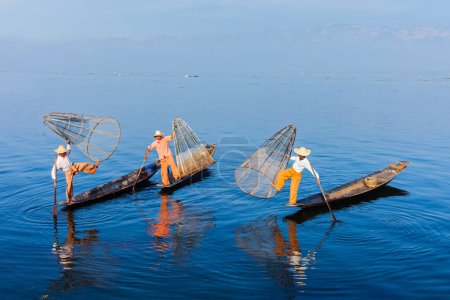 Myanmar travel attraction landmark - Traditional Burmese fishermen balancing with fishing net on boats at Inle lake in Myanmar. They are famous for their distinctive one legged rowing style.