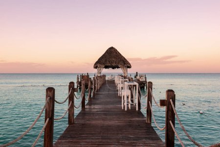 Téléchargez les photos : Belle plage des Caraïbes en République dominicaine. Coucher de soleil sur paysage tropical idyllique d'été avec de l'eau de mer bleue, ciel coloré et jetée en bois - en image libre de droit