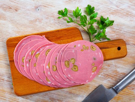 Appetizing italian sausage Mortadella with olives thinly sliced on wooden table