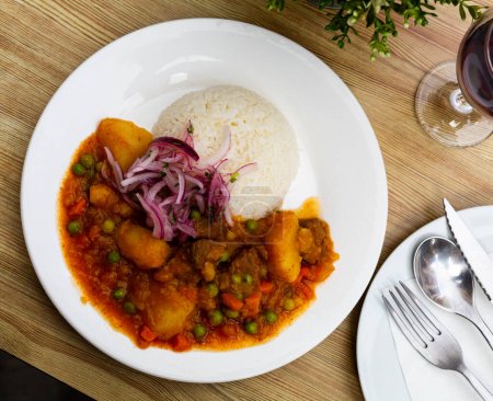 Dish of Peruvian cuisine, stewed meat with potatoes and peas, served with rice and onion at plate