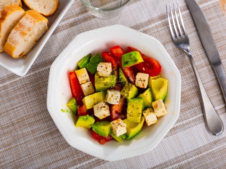 Traditional Mediterranean style salad from fresh ripe avocado with tomatoes and soft feta cheese seasoned with aromatic dried herbs and olive oil