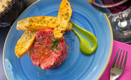Picture of raw veal steak tartar served at blue plate with fried toasts on cafe