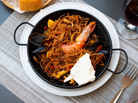 Köstliche traditionelle valencianische Fideua mit Meeresfrüchten, herzhafte Nudelgerichte mit Garnelen, Tintenfisch und Venusmuscheln, serviert in Paellera mit Sauce allioli
