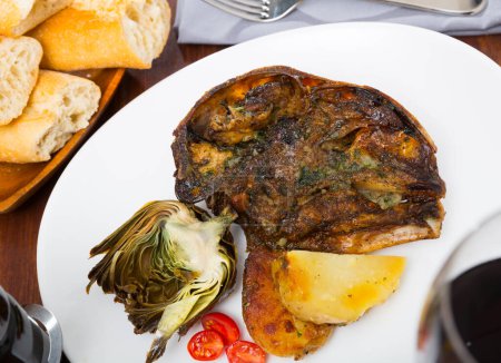 Roasted mutton head served with baked potatoes and halved artichoke and fresh tomatoes