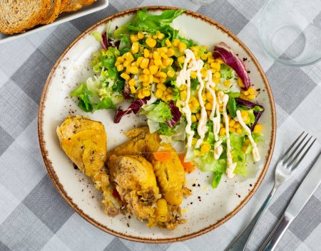 Delicious baked chicken pieces with side dish of vegetable salad with lettuce and canned corn kernels served for dinner
