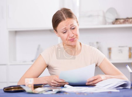 Junge Frau sitzt zu Hause und sorgt sich um Schulden auf Rechnungen