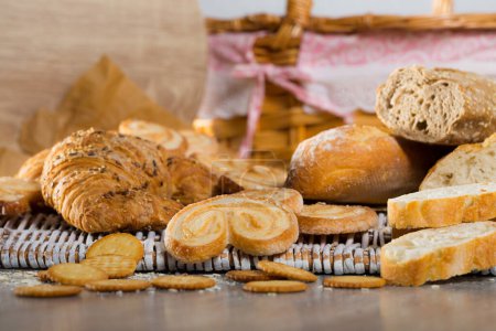 Assortment of fresh baked goods on wicker mat with basket on wooden background