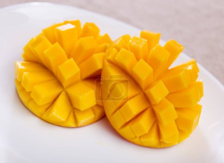 on table covered with tablecloth- two halves of ripe orange mango cut into cubes lie on white round plate.Isolated