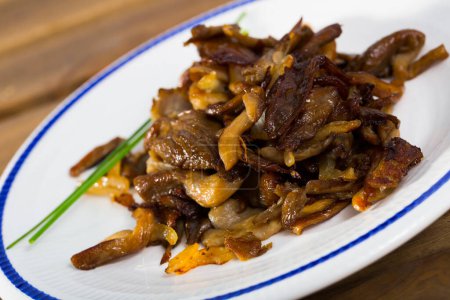 Cooked fried honey fungus mushrooms with onion and chives in white palte