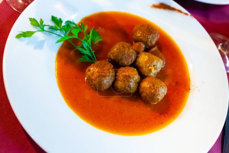 Close up of traditional spanish meatballs on white plate on red tablecloth