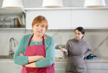 Fatiguée de travailler dans la cuisine, désolée mère en tablier écoute la conversation indignée de sa fille sur les réalisations insatisfaisantes de la vie