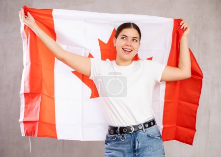 Young positive woman holding national flag of Canada in her hands