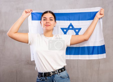 Porträt einer ernsthaften patriotischen jungen Frau mit der Nationalflagge Israels vor grauem Hintergrund