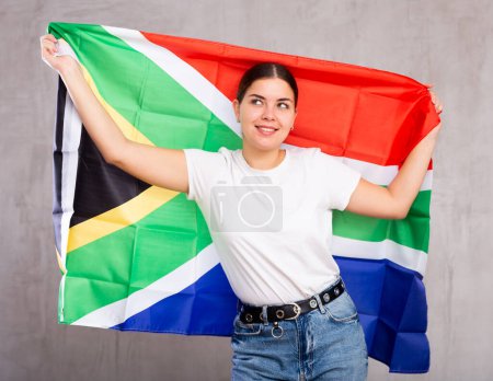 Joyeuse jeune femme avec le drapeau de l'Afrique du Sud dans les mains posant joyeusement sur fond unicolore clair