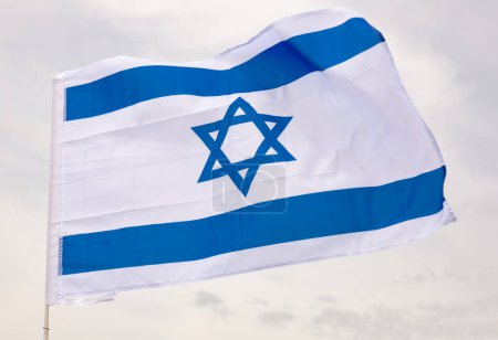 Gran bandera de Israel sujeta en palo contra el fondo del cielo azul bajo la luz del día