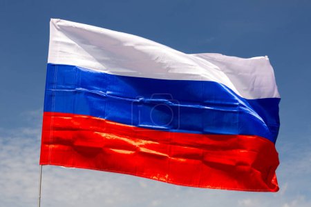 Close-up picture of national flag of Russian Federation waved in breeze on blue sky background