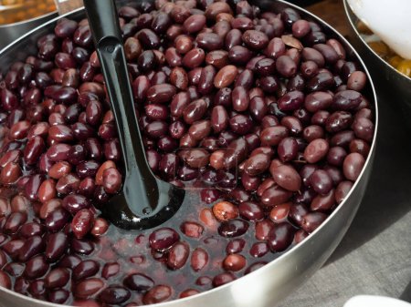 Pickled black olives scooped with skimmer out of bucket put on sale counter in the market
