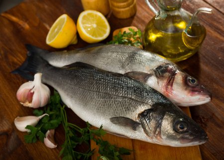 Raw sea basses with lemon, parsley, garlic and spices on cutting board on wooden background