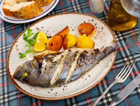 Delicious grilled gilthead bream dorada served with baked potatoes, slice of lemon and fresh greens